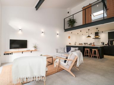 A living room with chairs and sofa facing a wall-mounted TV in an open plan space with a kitchen and dining area at Linden Barn in Wincanton
