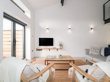 A living room with two armchairs facing a coffee table and TV mounted on the wall at Linden Barn in Wincanton