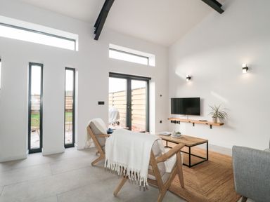 A living room with wooden chairs, coffee table, wall-mounted tv, and large windows at Linden Barn in Wincanton