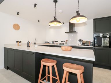 A kitchen with black cabinets white countertop wooden stools hanging lights and kitchen appliances at Linden Barn in Wincanton
