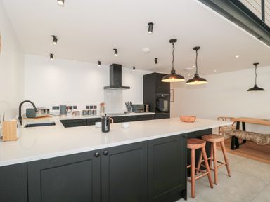 A kitchen with black cabinets white countertops wooden stools and a dining table with bench seating at Linden Barn in Wincanton