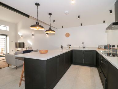 A kitchen with black cabinets white countertops hanging lights and a clock on the wall at Linden Barn in Wincanton