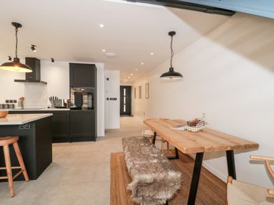 A kitchen and dining area with wooden stools and a table with a bench covered by a fur throw at Linden Barn in Wincanton