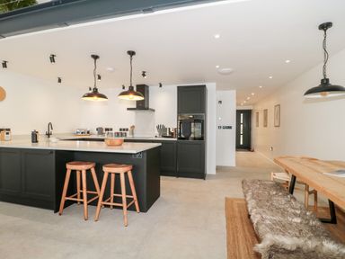 A kitchen with an island and two wooden stools next to a dining table with a bench covered in a fur throw at Linden Barn in Wincanton