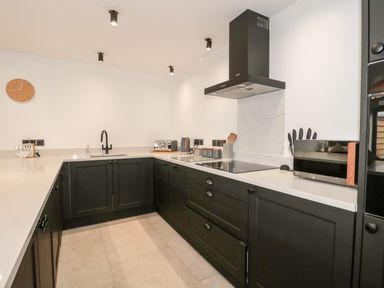 A kitchen with black cabinets white countertops a black stove and hood a sink toaster and knife holder at Linden Barn in Wincanton