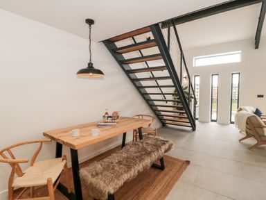 A dining area with a wooden table and chairs under stairs in a modern room with large windows at Linden Barn in Wincanton