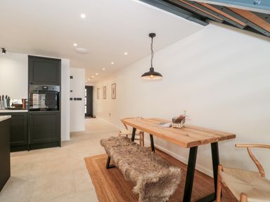 A dining area with a wooden table, a bench with a fur cover, and two chairs at Linden Barn in Wincanton
