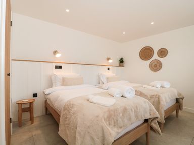 A bedroom with two single beds side by side each with white linens and beige throws at Linden Barn in Wincanton