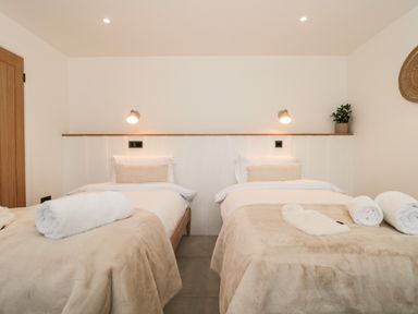 A bedroom with two single beds with beige blankets and white towels at Linden Barn in Wincanton