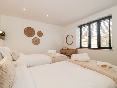 A bedroom with two single beds white bedding and rolled towels on a beige throw a wooden desk with a round mirror and window blinds at Linden Barn in Wincanton
