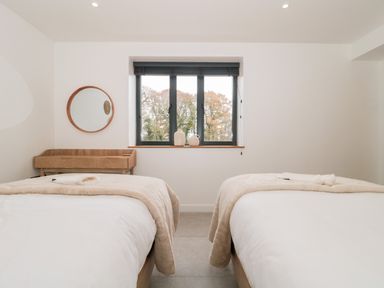 A bedroom with two beds a wall mirror a window with three panes and two vases on the windowsill at Linden Barn in Wincanton