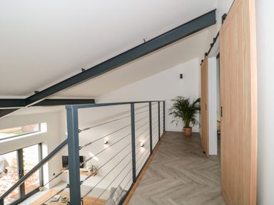 A hallway with wooden sliding doors a potted plant and metal railing overlooking a living area at Linden Barn in Wincanton