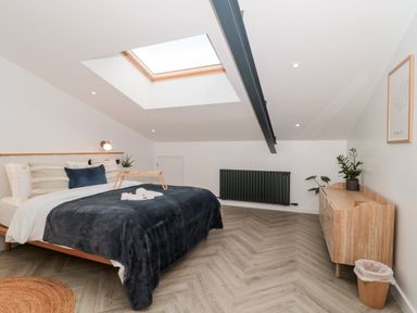A bedroom with a skylight above the bed and a wooden dresser with plants and a waste bin at Linden Barn Wincanton