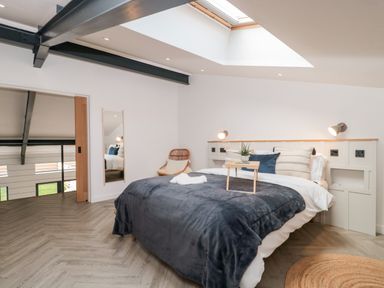 A bedroom with a bed covered in blue and white linens a small table a chair and a skylight at Linden Barn in Wincanton