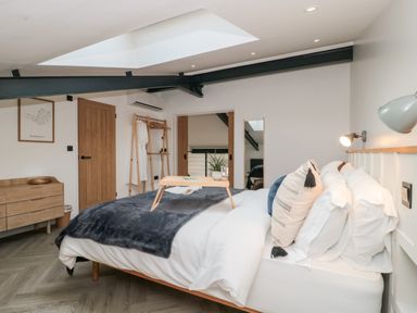 A bedroom with a bed, pillows, a blanket, a wooden dresser, a wooden door, a clothes rack, a wall mirror, and a skylight at Linden Barn in Wincanton