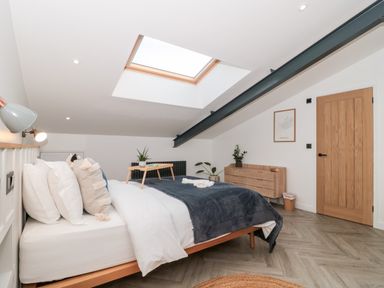 A bedroom with a bed a skylight a wooden dresser and a wooden door at Linden Barn in Wincanton