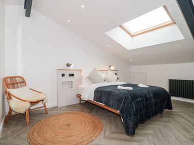 A bedroom with a double bed pillows and blankets a wicker chair with cushions a circular rug and a skylight window at Linden Barn in Wincanton