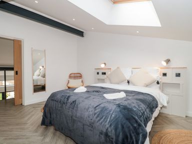 A bedroom with a double bed covered with a dark blanket and pillows beside a wall with reading lamps at Linden Barn in Wincanton