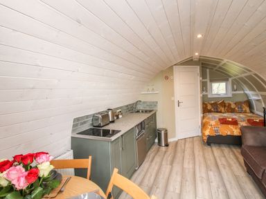 A compact living space with a kitchenette, dining table with flowers, bed, and sofa at Cherry Pod 2 in Hookagate near Meole Brace