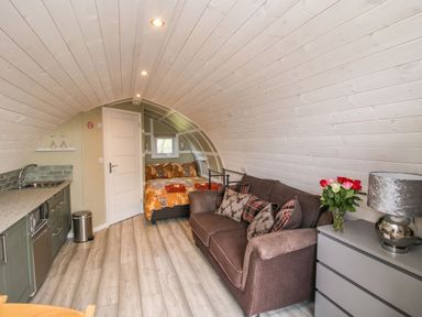 A small living space with a brown sofa and patterned pillows near a bed with orange bedding in Cherry Pod 2 Hookagate near Meole Brace