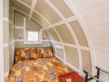 A bedroom with a bed under a small window inside a curved wall at Cherry Pod 2 in Hookagate near Meole Brace