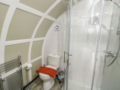 A bathroom with a toilet covered by an orange cloth a glass shower enclosure and a towel radiator at Cherry Pod 2 in Hookagate near Meole Brace