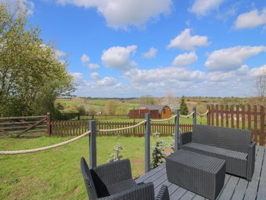 An outdoor patio area with black wicker furniture and fenced green field at Cherry Pod 2 Hookagate near Meole Brace
