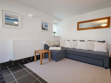 A sitting area with a gray sectional sofa and white pillows a wooden side table a wall mirror and framed pictures at The Mill in Trethevy near Tintagel