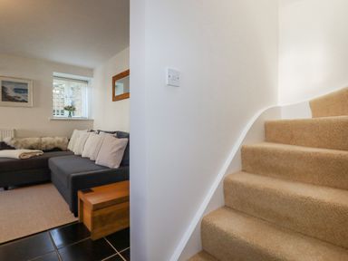 A stairway with carpet beside a living room with a sofa and cushions at The Mill in Trethevy near Tintagel
