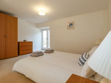 A bedroom with a bed linens on the bed wooden wardrobe and chest of drawers with folded towels by the door at The Mill in Trethevy near Tintagel