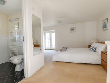 A bedroom with a bed beside two bedside tables a door leading to a balcony and an adjoining bathroom at The Mill in Trethevy near Tintagel