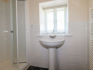 A bathroom with a shower enclosure pedestal sink soap dispenser window with blinds and white tiled walls at The Mill in Trethevy near Tintagel