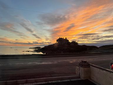 A coastal view at sunset with a house on a rocky outcrop beside the sea at Porth Ewyn in Trearddur Bay