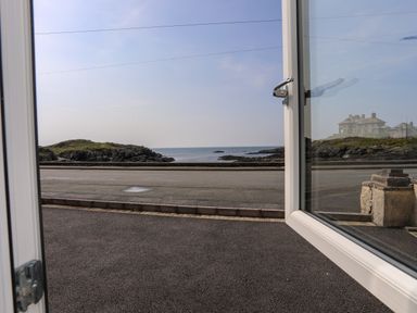 An open door showing a view of a road grassy rocky coastline and the sea at Porth Ewyn in Trearddur Bay