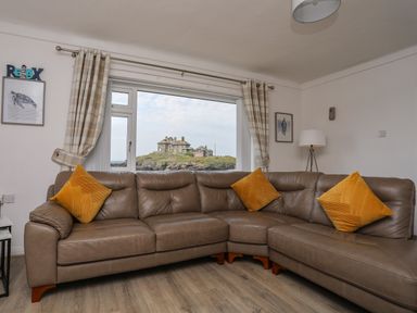 A living room with a brown leather corner sofa and yellow cushions a floor lamp checked curtains and framed pictures on the wall at Porth Ewyn in Trearddur Bay