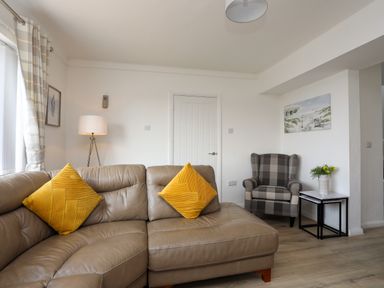 A living room with a leather sofa with yellow pillows a plaid armchair and a side table with flowers at Porth Ewyn in Trearddur Bay