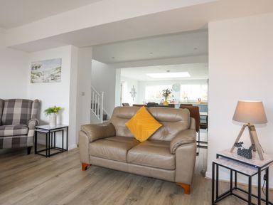 A living room with brown leather sofa with a yellow cushion and a checkered armchair with side tables and a lamp at Porth Ewyn in Trearddur Bay