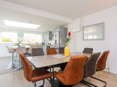A dining area with a table and chairs next to a kitchen with bar stools and appliances at Porth Ewyn in Trearddur Bay