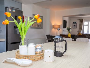 A kitchen area with a vase of orange tulips a French press and cups on a table at Porth Ewyn in Trearddur Bay