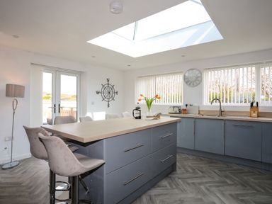 A kitchen with an island counter and bar stools with windows and a skylight at Porth Ewyn in Trearddur Bay
