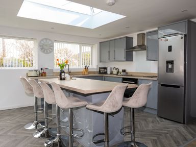 A kitchen with a central island and bar stools a refrigerator and cabinets at Porth Ewyn in Trearddur Bay