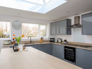 A kitchen with grey cabinets a wooden countertop a sink a built in oven a microwave and flowers in a vase at Porth Ewyn in Trearddur Bay