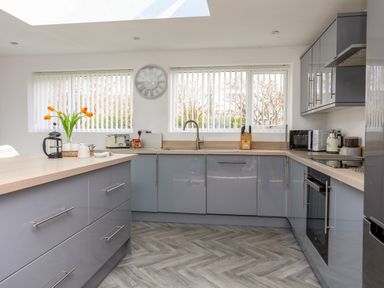 A kitchen with grey cabinets a wooden countertop a sink microwave oven and flowers on the counter at Porth Ewyn in Trearddur Bay