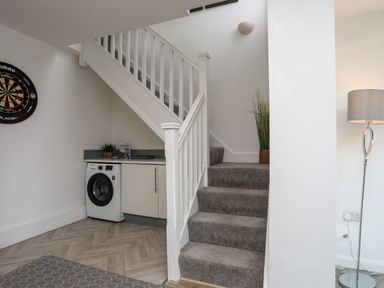 A staircase with carpet leading up next to a washing machine and cabinet under the stairs at Porth Ewyn in Trearddur Bay