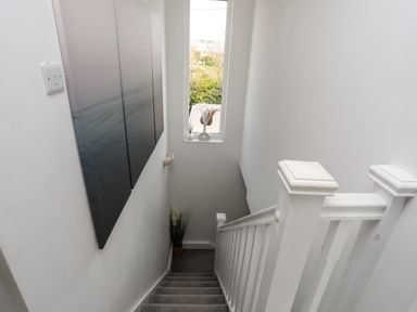 A staircase with carpeted steps and white wooden railing with a tall window and wall art in Porth Ewyn Trearddur Bay
