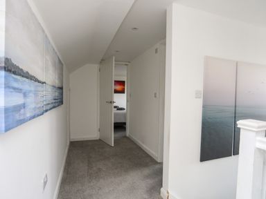A hallway with gray carpet and white walls leading to a bedroom with the door partially open at Porth Ewyn in Trearddur Bay