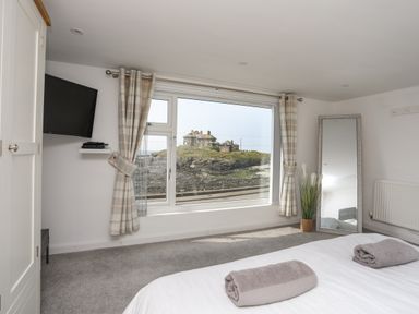A bedroom with a large window showing a house outside a wall mirror and a mounted television at Porth Ewyn in Trearddur Bay