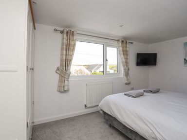 A bedroom with a bed, towels on the bed, window with curtains, radiator, wall-mounted television, and wardrobe at Porth Ewyn in Trearddur Bay
