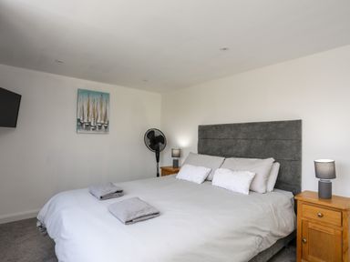 A bedroom with a bed with pillows and towels bedside tables with lamps a wall fan and a painting at Porth Ewyn in Trearddur Bay