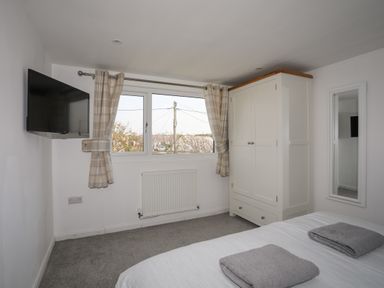 A bedroom with a wall-mounted television curtains on a window a radiator a white wardrobe a mirror and a bed with towels at Porth Ewyn in Trearddur Bay